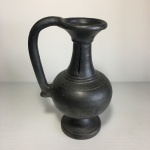 Ânfora em metal cinzelado, decorada com detalhes incrustados e fendas na parte superior. Dimensões: 20 cm.