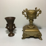 Duas antigas e pequenas ânforas decorativas de metal. Dimensões: 19 cm x 12 cm x 12 cm (maior peça).