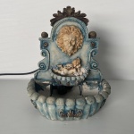 Fonte de água, decorativa, de resina, decorado com cabeça de leão e querubim. Funcionando. Dimensões:23 cm x 18 cm x 20 cm.
