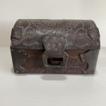 Antigo e pequeno baú feito de couro,  decorado com estilizados em baixo relevo. Dimensões: 13 cm x 14 cm x 19 cm.