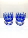 Dois copos de cristal lapidados, translúcido e azul. Um copo com ínfimo bicado na borda. Dimensões: 9 cm.
