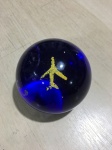 Peso para papel em pasta de vidro com figura de avião no interior. Presença de batidas. Dimensões: 4 cm.