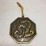 Pendurador para porta em bronze, formato octogonal, com imagem de serpente em alto relevo. Dimensões: 10 cm.