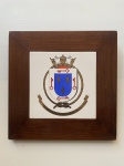 Quadro de madeira e placa de cerâmica esmaltada, decorado com brasão ao centro. Dimensões: 25 cm x 25 cm.