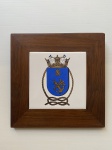 Quadro de madeira e placa de cerâmica esmaltada, decorado com brasão ao centro. Dimensões: 25 cm x 25 cm.