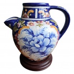 Imponente e bojuda jarra em cerâmica Luis Salvador, vitrificada e policromada com motivos florais, modelo Alcobaça Madalena, acompanha peanha em madeira, apresenta lascado no bico. Med. Alt. 30cm