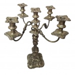 Candelabro para cinco lumes, confeccionados em metal espessurado a prata, corpo com expansão próximo a base e formato balaústre cinzelada em gomos e arabescos, braços em curva finalizando com bobeches soltas cinzelada em forma de flor, base quadrangular decorada com relevo. Necessita restauro. Med. 31x30x47 cm. Desgastes e marcas do tempo.