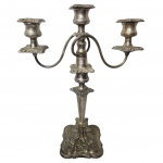  Candelabro para três lumes, confeccionados em metal espessurado a prata, corpo com expansão próximo a base e formato balaústre cinzelada em gomos e arabescos, braços em curva finalizando com bobeches soltas cinzelada em forma de flor, base quadrangular decorada com relevo. Med. 33x13x40 cm. Desgastes e marcas do tempo. 