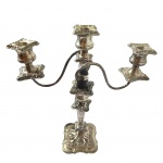  Candelabro para três lumes, confeccionados em metal espessurado a prata, corpo com expansão próximo a base e formato balaústre cinzelada em gomos e arabescos, braços em curva finalizando com bobeches soltas cinzelada em forma de flor, base quadrangular decorada com relevo. Med. 33x13x40 cm. Desgastes e marcas do tempo. 