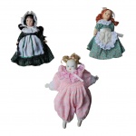 MEMORABILIA - Duas miniaturas de bonecas de coleção com cabeça, corpo, pernas e braços em porcelana, cabelos e roupas de época e um bebê com macacão de lá com corpo de pano, cabeça, braços e pernas em porcelana. Med. 15 cm alt.