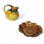 Duas peças em cerâmica, sendo um centro de mesa com patina dourada bordas onduladas, apresenta restauro e fio de cabelo e um bule com policromia sobre fundo amarelo. Med. Alt. 7, diam. 22cm e Alt. 15cm, diam. 13cm