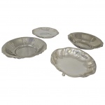 Quatro travessas circulares em metal espessurado a prata com bordas onduladas, uma apoiada em pés bola. Med. Diam. 19 a 21cm