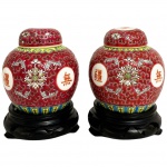 CHINA - Par de potiches em porcelana oriental fartamente adornados com motivo floral sobre fundo magenta, apoiados sobre peanhas de madeira entalhadas. Possui registro na base. Uma das tampas com sinal de restauro. Mede 15cm altura cada.