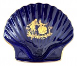 LIMOGES FRANÇA - Petisqueira em pasta de porcelana francesa LIMOGES, adornada com cena galante em vibrante ouro sobre fundo azul cobalto. formato concha. Possui registro da manufatura. Mede 12 x 13cm.