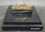 Miniatura em prata de lei contrastada teor 925 mile, com banho de ouro, representando barco- base em resina negra com a inscrição "pink fleet"- barco med. 2,5x5 cm e base med. 3,5x9x9