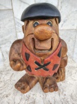 Escultura em madeira maçica representando FRED FLINTSTONE. A série dos  FLINTSTONES  foi ao ar pela primeira vez em 1960 , sendo  um sucesso tanto para adultos quanto para crianças e é conhecida  por seu humor e personagens cativantes . A escultura e´grande e mede  24 x 14 x 31 cm.