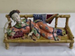 Grupo escultórico representando figura feminina apoiada em sofá  em cerãmica policromada com detalhes em biscuit . Faltam dois dedinhos. comprimento 27 cm , profundidade 10 cm e altura 10 cm