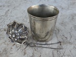 Duas peças em metal prateado: um coador para chá e um copo CHRISTOFLE, medindo 8 x 7 cm.