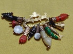 JÓIA DE CRIOULA - Rara penca de balangandãs ( propiciatório ) de ouro baixo sustentando  onze peças tipo figas em coral , peixes , figuras de condomblé  em pedras e materiais diversos todos guarnecidos com ouro amarelo  .Bahia . Século XIX  .11 X 7 cm. Aproximadamente 21 gramas.