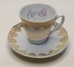 Conjunto de Porcelana Floral com Detalhes Dourados  Elegância e DelicadezaEncante-se com este refinado conjunto de porcelana composto por xícara e pires em tom branco, com bordas realçadas em dourado e delicadas flores pintadas no interior da xícara. A combinação entre o acabamento clássico e a arte floral em tons de roxo e verde confere à peça um toque romântico e sofisticado.