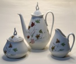 Conjunto de Porcelana Decorada com Folhagens Outonais  Elegância e Charme para Servir Apresentamos um delicado trio composto por bule, açucareiro e leiteira  todos em porcelana branca com estampa exclusiva de folhas em tons de verde, vermelho e marrom, evocando a beleza nostálgica do outono.