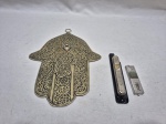 Lote judaico em metal dourado, composto de mão de Deus e mezuzah em metal. Medindo a mão de Deus 22cm x 18cm.