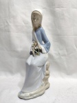LLADRÓ - Escultura de coleção em porcelana espanhola policromada representando "Dama com copos de leite". Peça marcada, selada e numerada na base. Medindo 24cm de altura. Com leve restauro no buque de flores.