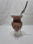 Cuia de chimarrão em cabaça com bomba em metal prateado e dourado, com suporte. Medindo 18cm de altura total da cuia no suporte.