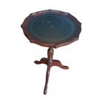 Mesa de apoio antiga, em madeira nobre, estilo inglês, tampo revestido em couro (com leve mancha), bordas recortadas apoiada em coluna torneada sustentada por pernas tripóides, Diam. 32, Alt. 61 cm.