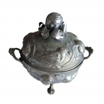 Sopeira em  estanho ricamente repuxada em pássaros e frutas com pega em esfera adornada com lâminas representando pétalas, apoiada em pernas de garras de animal, Alt. 24, Diam. 19 cm. parte interna e base externa apresentam leve desgaste do metal, Diam. 19 cm. Alt. 24 cm.
