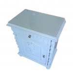 Mesa de cabeceira em madeira nobre patinada de branco, tampo com protetor de vidro,  com uma gaveta e uma porta central,  sustentado por colunatas, apliques em alto relevo, puxadores de cobre, 51 x 32, Alt.63 cm.
