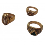 Três anéis em metal dourado com pedras: verde, uma tipo topázio (este com o metal com pequeno lascado) e  um cristal, aros 16, 21 e 24.