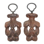 Par de originais arremates decorativos em madeira esculpida, vazada e ornada por frisos florais e adornos estilizados. Topos com argolas ovaladas em metal. 26 x 12 cm.