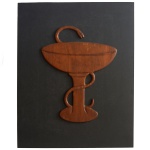 Elemento em madeira entalhada representando o símbolo da farmácia. 32 x 25 cm (MI). 48 x 40 cm (ME).  No símbolo de farmácia, a taça e a serpente carregam significados profundos. A taça representa a cura e a serpente, representa o poder, a ciência e a sabedoria. O uso desses elementos pode ser compreendido através da mitologia grega, especificamente no que diz respeito à história de Asclépio, o deus da medicina, e de sua filha Hígia ou Higeia (Salus para os romanos), a deusa da saúde.