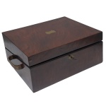 Secretária de mesa retangular em rádica escura, construída em 2 partes. Metade superior reclinável, formando plano de escrita revestido em couro azul, encimado por faixa com porta canetas escavado e ladeado por tinteiros em cristal. Alças laterais em argola. Séc. XIX. 16 x 37 x 25 cm (fechada). 12 x 51 x 37 cm (aberta). Sinais de uso e do tempo.