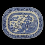 W.RIDGWAY  Travessa ovalada em faiança, semi-porcelana, decorada em azul. Apresenta larga margem ornada por faixa com adornos geométricos e florais. Centro ornado por paisagem lacustre ao gosto chinês, com edificações, barcos, figuras, salgueiros e aves. Marca da manufatura no verso. 34 x 28 cm.