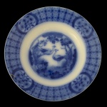 JOHNSON BROTHERS  Prato raso em porcelana inglesa, decorado em azul. Apresenta larga margem com padrão geométrico realçado por reservas florais. Centro ornado por casal de aves em jardim florido. Marca da manufatura e do modelo Mongolia no verso. Fio de cabelo no verso. 23 cm.