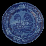 Prato raso em porcelana inglesa, decorado em azul. Apresenta borda ondulada realçada por fino friso geométrico. Margem com flores, folhagens e frutas, centralizando paisagem campestre com montanhas, castelo, figuras e animais, 25 cm.