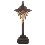 Séc, XIX - Imagem em madeira policromada de Cristo Crucificado. Apresenta-se N. Senhor Jesus, de cabeça caída, vestindo o tradicional cendal. Cruz escura e lisa, com hastes rematadas em ponteiras, centralizando disco solar com folhagens na parte inferior. Base retangular em degraus. Defeitos na cruz). Séc. XIX. 41 x 16 cm (cruz). 14 x 10 cm (Cristo).