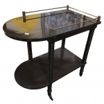 Carrinho de chá em madeira nobre, construído com 2 plateaux superpostos, de formato retangular tendo uma das extremidades em meia lua. Galeria superior aberta, montada com hastes em metal dourado. Pernas retas e aneladas, rematadas por rodinhas. Design Anos 70. 74 x 74 x 43 cm.