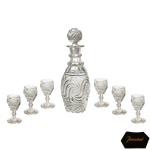 BACCARAT - Elegante e original conjunto de licoreiro e 6 cálices em cristal francês lapidado. Bojo abaulado, com base moldada e ornada em gomos torcidos, encimada por larga faixa com ondas espiraladas centralizando medalhões. Gargalo facetado em corneta, interrompido por anelados e rematado por borda revirada. Tampa esférica no estilo. Copos cônicos repetindo as ondulações, apoiados em hastes aneladas sobre pés circulares. 23 cm (licoreiro). 9 cm (cálices).