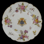 MEISSEN - Prato em porcelana com borda ondulada e dourada, profusamente ornado em policromia com arranjos e adornos florais. Apresenta ao centro brasão de armas com flores de lis sob coroa, ladeado por composições florais. No verso, marca da manufatura. Séc. XIX. 26 cm.