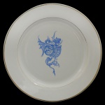 FÁBRICA DE ALCANTARA  LISBOA - Prato em faiança portuguesa branca, com borda circular lisa. Centro ornamentado por sofisticada composição pictórica em esmalte azul. Apresenta belo dragão alado, segurando brasão de armas sob coroa, decorado com 7 torres e pequeno brasão com 5 escudos do rei D. Manuel ao centro. No verso, marca da manufatura. 23 cm.