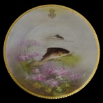 VIEUX PARIS - Prato em porcelana francesa policromada com borda dourada, ornamentado por peixes sobre fundo florido. Apresenta monograma na margem. Marca da casa comercial E. Bourgeois  Paris  Marseille, sob a base. 25 cm.