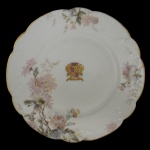BARÃO DE PORTO FELIZ  Prato raso em porcelana europeia policromada, pertencente ao Serviço do primeiro e único Barão de Porto Feliz (Cândido José de Campos Ferraz - Campinas, 1830 - Rio Claro, 1880). Apresenta borda recortada e filetada em dourado. decorada em alto relevo com ramos de flores, e ao centro o brasão com armas. França. Século XIX. Marca da manufatura Limoges Haviland ao fundo. 20 cm. Fazendeiro e político brasileiro, líder do Partido Conservador na região de Limeira, São Paulo, e fundador da colônia agrícola de Boa Vista.