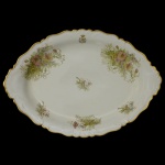 LIMOGES  Travessa oval em porcelana francesa branca com borda movimentada e dourada. Apresenta ornamentação com arranjos florais, encimados no topo por monograma sob coroa. Marca da manufatura sob a base. 42 x 30 cm. Apresenta restauro.