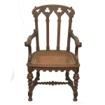 Original e bela cadeira de braços em madeira nobre, com influência neogótica. Encosto reto, com traves verticais rematadas por adornos vazados no formato de corações, e encimadas por cachaço arqueado em voluta. Braços ondulados, apoiados sobre assento revestido em palhinha da Índia. Saia recortada em arcos. Pernas retas e torneadas ornadas por anelados e torsades. Base com amarração em H, seguindo o estilo.. 97 x 56 x 50 cm. Sinais de uso e do tempo.