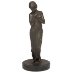 Estatueta em bronze patinado representando figura feminina de pé sobre base circular em mármore preto. 38 x 16 cm.