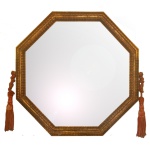 Espelho de parede de formato octogonal, bordado por moldura em madeira dourada, lavrada com canelados e realçada nas laterais por pompons em passamanaria.  51 x 51 cm (MI). 61 x 61 cm (ME).