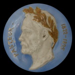 EDMOND LACHENAL (1855-1930)  Medalhão em faiança esmaltada azul. Apresenta ao centro, em baixo-relevo de cor branca, cabeça perfilada do cientista Louis Pasteur, famoso fundador da microbiologia. Exibe, em dourado, coroa de louros na cabeça e borda com os dizeres Pasteur (1822 -1895). Assinado.23 cm.